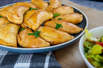 Traditional Latin American baked beef empanadas on a plate with a fresh salad sidedish. Gluten free savory pastries with meat beef stuffing or filing. Handmade Typical dish in Spain or Argentina.