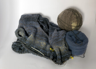photo with knitting needles, balls of yarn and a piece of knitted jacket on a solid white background