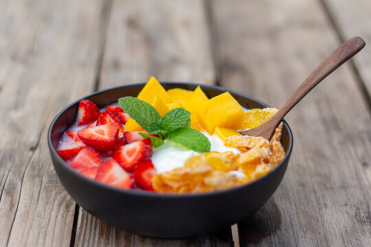 greek yogurt with mango strawberrise conflex in black bowl on wooden table top view