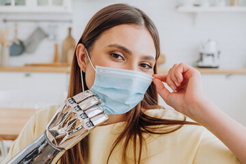 Positive lady puts on blue disposable protective mask by modern metal bionic prosthesis arm in...