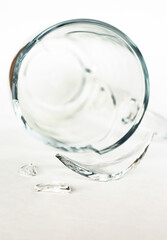 broken transparent empty cup on white background, shards of glass closeup, crash and accident concept