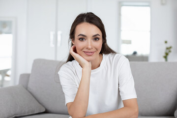 Smiling happy woman sitting on the couch at home while online communication look at camera,
