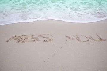 Text on sand beach Miss You. with blue sea and soft wave at coast. broken heart or tourist travel summer in holidays concept.