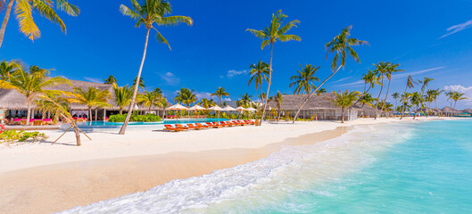 Luxurious beach resort with swimming pool and beach chairs or loungers under umbrellas with palm trees and blue sky. Summer island travel and vacation destination. Relax lifestyle, leisure carefree