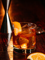 a glass of whiskey with an ice cube and orange peel decor. On a wooden bar