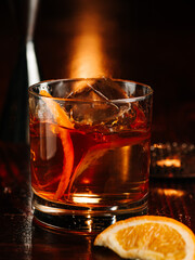 a glass of whiskey with an ice cube and orange peel decor. On a wooden bar