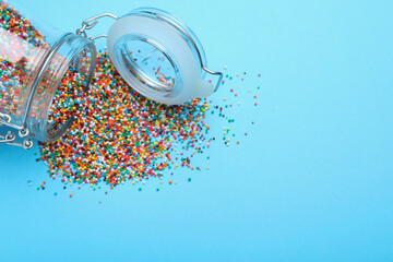 Colorful sprinkles and jar on light blue background, flat lay with space for text. Confectionery decor