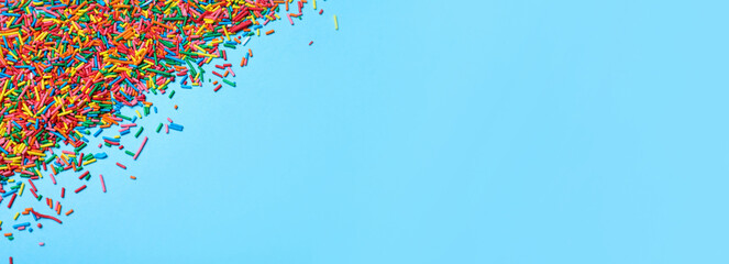 Colorful sprinkles on light blue background, flat lay with space for text. Confectionery decor