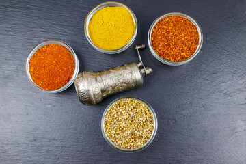Set of different aromatic spices and spice mill on black slate. Top view
