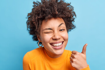 Happy positive African American woman smiles broadly makes okay gesture with thumb up says its...