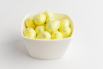 Yellow chocolate coated Easter eggs candies on a bowl isolated on a white table, tasty sugary dessert for children.