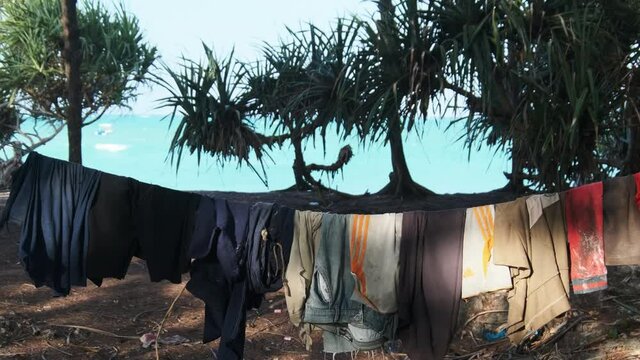 Clothes are dried on a rope in a poor African village. Various Colourful clothes, T-shirts, pants hanging out to dry on a clothesline between the palm trees. Lot of Washings are drying outside. Africa
