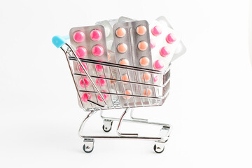 Many medicine pills, tablets and vitamins in a small supermarket shopping cart isolated on white background, pharmaceutical picture taken with soft focus.