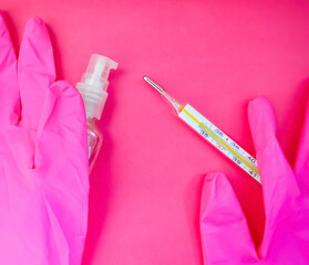 Mercury thermometer, pink medical gloves and sanitizer on pink background with copy space. Medical equipment theme. Health care system background.