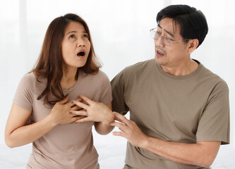 Portrait shot of senior Asian lover couple wearing eyeglasses. Wife suffering from cardiac chest pain caused by her cardiovascular diseases with a worried husband looking and supporting her with care.
