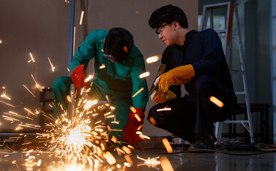 two Asian engineer wearing a mechanic jumpsuit, safety eyeglasses, and gloves working carefully in a workshop of a factory. Senior mechanic training a new worker with concern