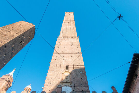 The tower Torre Asinelli in Bologna from below photographed in the sunshine against a blue sky with cables graphically in the foreground