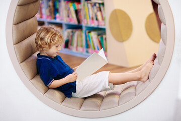 Child in school library. Kids reading books.