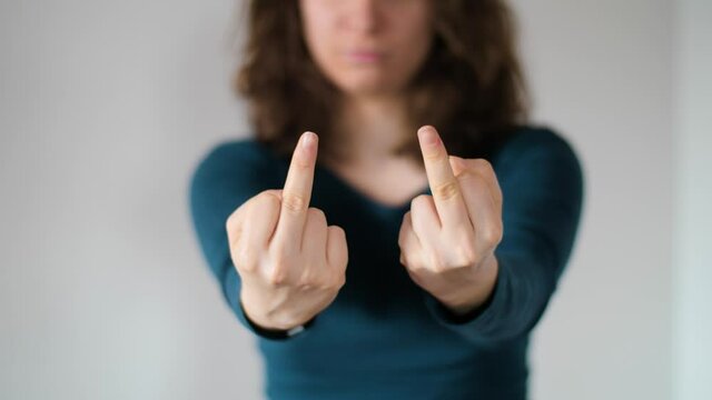 Woman showing two middle fingers with her hands in front of a white background. Isolated close-up of offensive, rude and insulting gesture in slow motion. Concept of provocation and aggression. 4K.