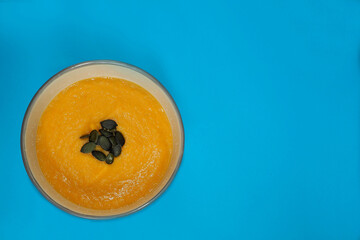 cream soup of pumpkin and carrot with pumpkin seeds stands in a round gray plate on a blue background top view . homemade food