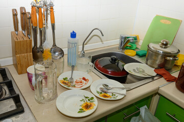 A pile of unwashed dishes on the kitchen table with a sink