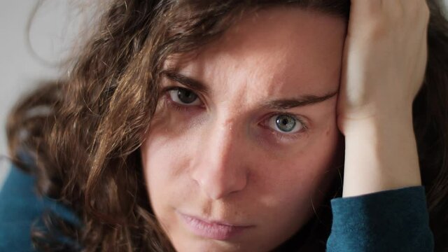Close up portrait of beautiful annoyed young woman looking at the camera. Gorgeous Caucasian girl with pretty face and blue eyes and intense angry stare resting on hand. Slow-motion, 4K.