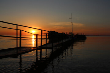 Obraz premium old pier bridge to the ship at sea at sunset with a mast