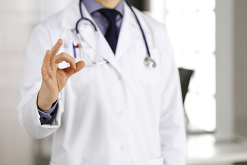Unknown male doctor standing straight with OK sign in clinic near his working place, closeup. Perfect medical service in hospital. Medicine and healthcare concept