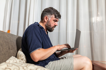 bearded man on sofa uses laptop in dining room overnight