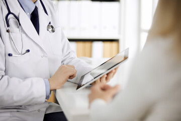 Unknown male doctor and patient woman discussing current health examination while sitting in clinic...
