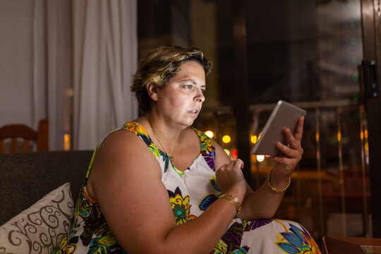 Overweight Woman Sitting On The Sofa With Tablet In Hand,