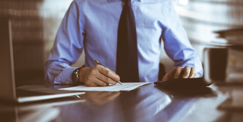 Unknown man accountant in blue shirt use calculator and computer with holding pen on while staying at home during covid pandemic. Taxes and audit concept