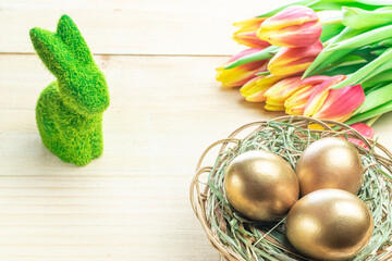 Easter symbol. Golden eggs in basket with spring tulips, white feathers on wooden background in Happy Easter decoration. Congratulatory easter design.