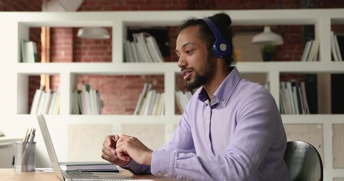 African businessman sit at workplace desk wear headphones communicate to client remotely use laptop and videoconference app. Student and webinar activity. Video call event, modern tech usage concept
