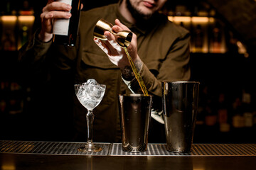 front view on shaker cups and glass on bar counter and bartender pouring drink