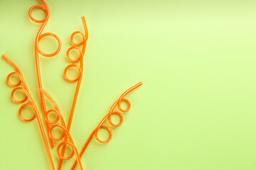 Orange plastic drinking straws on green background, flat lay. Space for text