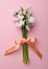 Beautiful bouquet of snowdrops on pink background, top view
