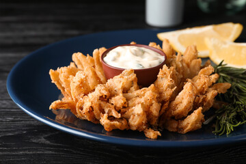 Fried blooming onion with dipping sauce served on dark wooden table, closeup