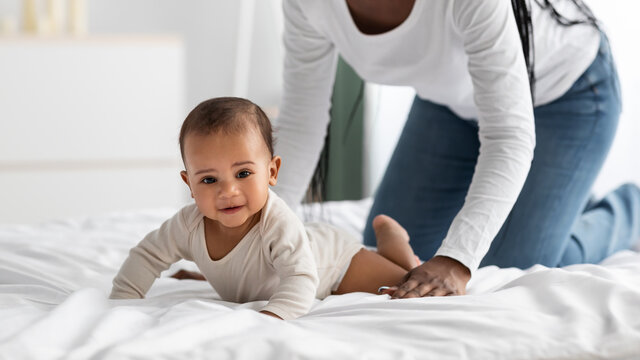 Cute little African American baby crawling in bed with mum
