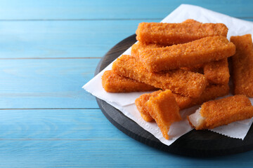 Fresh breaded fish fingers served on light blue wooden table, space for text