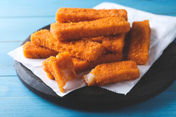 Fresh breaded fish fingers served on light blue wooden table