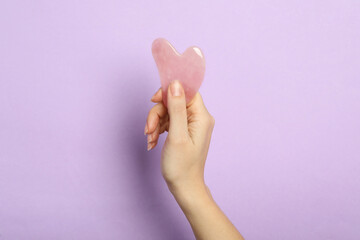 Woman with rose quartz gua sha tool on lilac background, closeup