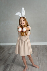 Teenage holding white eggs on grey background. Holidays, spring, Easter, minimalistic concept. Home Portrait of lovely, smiling girl in rabbit ears in beige dress celebrating Easter day. copy space