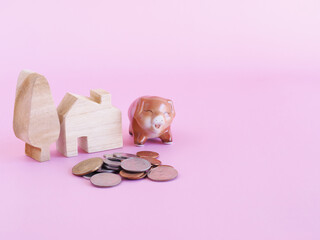 Brown ceramic piggy with wooden toy house, tree and coins pile on pink color background. Space for your text, Saving money, investment, business concept..