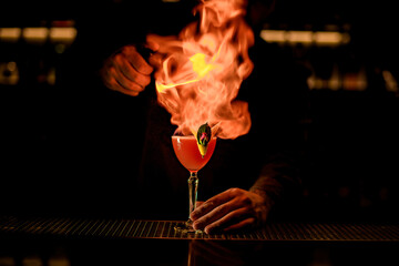 view of glass with cocktail that bartender sets to fire at dark bar