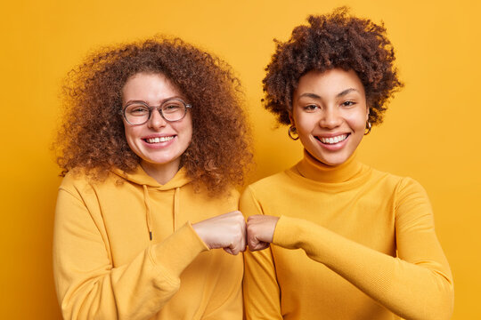 Two happy diverse women make fist bumps demonstrate agreement have friendly relationship smile gladfully stand next to each other isolated over yellow background. Teamwork body language concept - Powered by Adobe