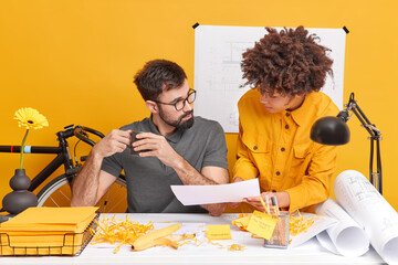 Mixed race woman trainee and chief man designer colleagues discuss ideas for future project during coffee break collaborate as one team share optinions about how to improve sketches pose at workplace
