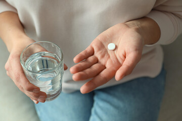 Young woman with abortion pill and glass of water on sofa, closeup - obrazy, fototapety, plakaty