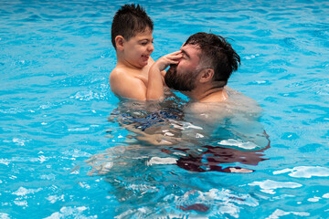 child with disability laughs and plays in his father's arms in a swimming pool