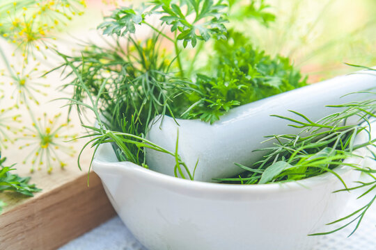 Mortar and pestle with fresh green herbs spices. Fresh dill, parsley, arugula and garlic on wooden board and white towel.